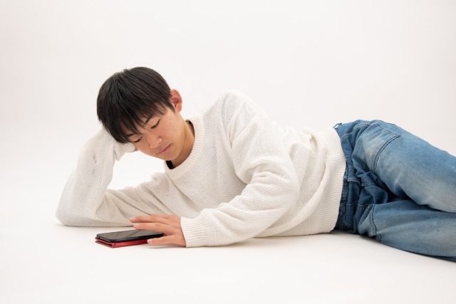 寝転ぶながら携帯を触る男
