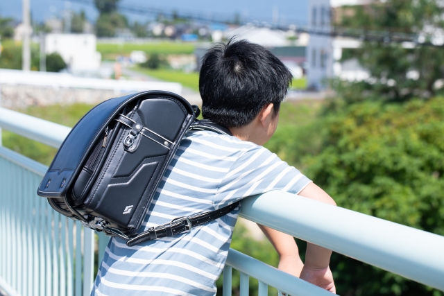 ランドセルを背負い橋の下を眺める男の子