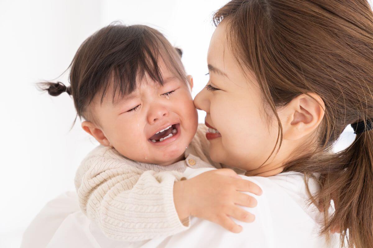 泣いている赤ちゃんを抱きかかえる保護者の様子。